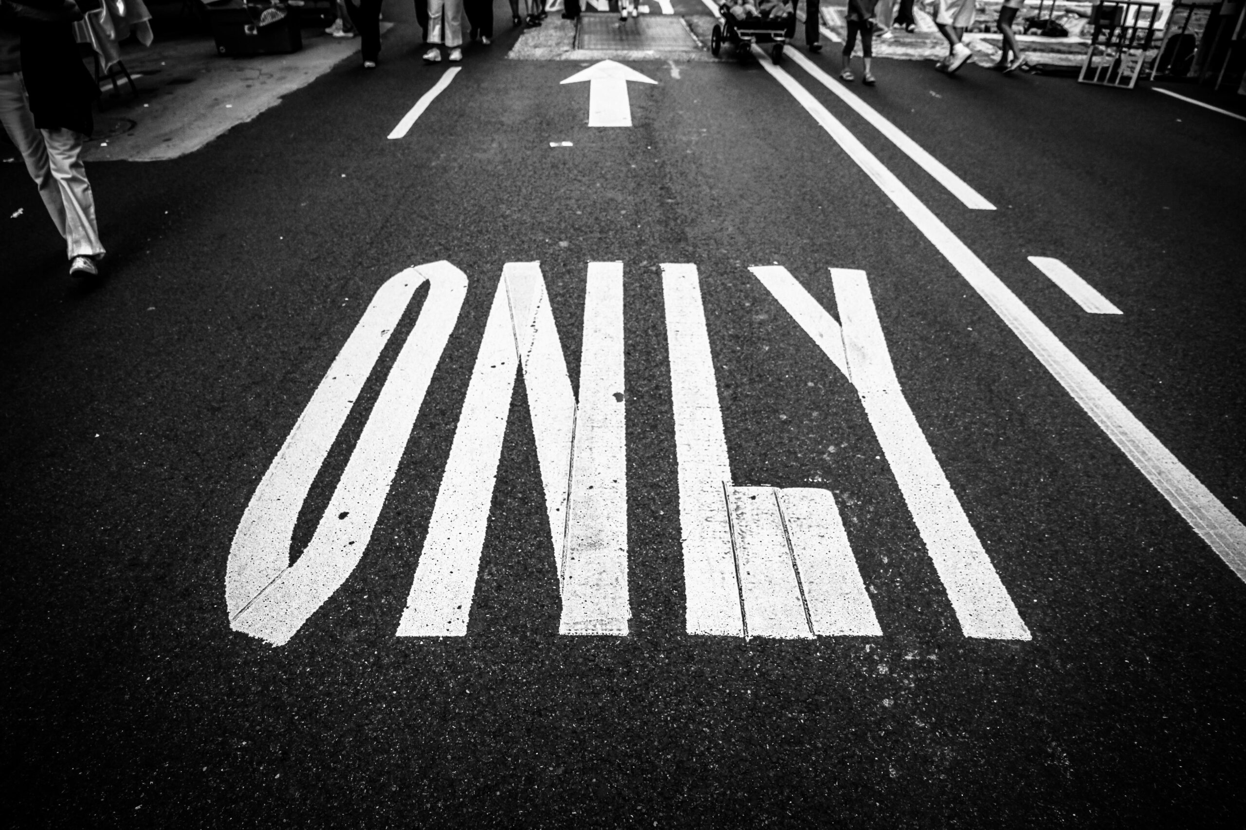 Black and white photo of road, showing traffic markings, a crowd, and an arrow.